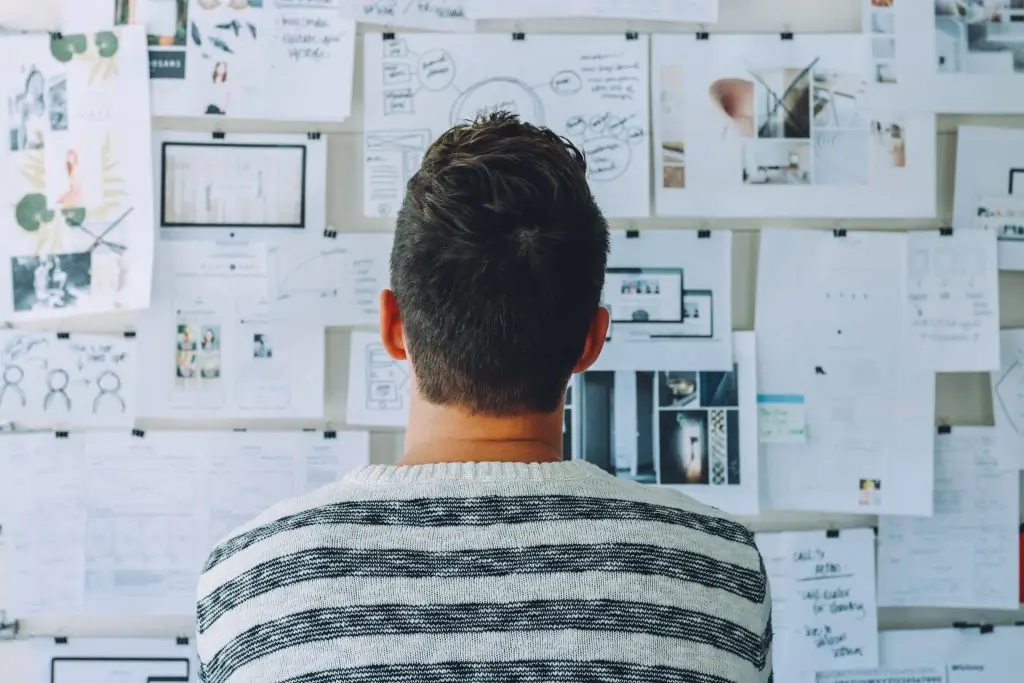 Someone seen from behind studying a wall covered in pinned notes and printouts