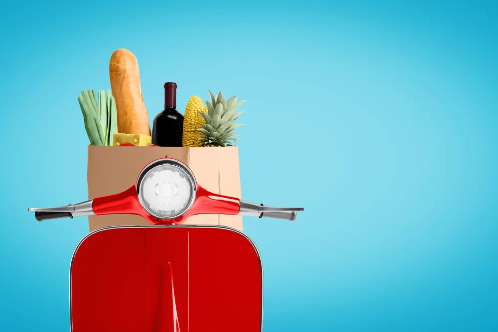 A red scooter carrying a paper bag of groceries, a baguette and pineapple poking out
