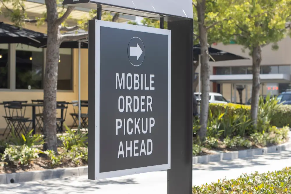 A sign outside a shopping plaza reads “Mobile order pickup ahead” with an arrow pointing the way