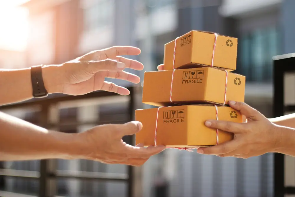 Hands passing a stack of three parcels marked Fragile to another pair of waiting hands