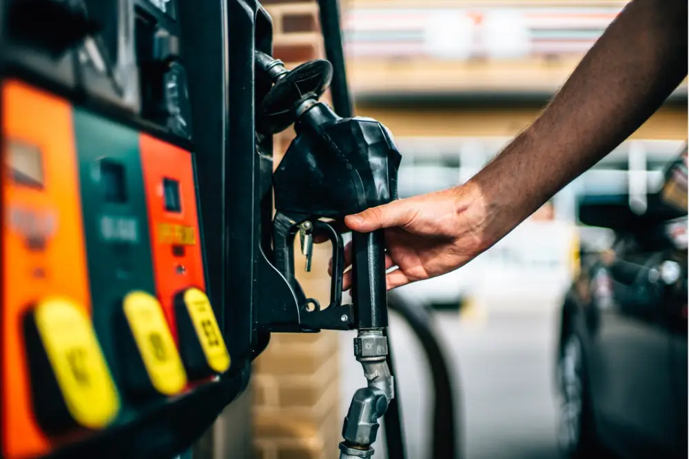 A hand reaching for a fuel nozzle at a gas station pump with coloured grade buttons