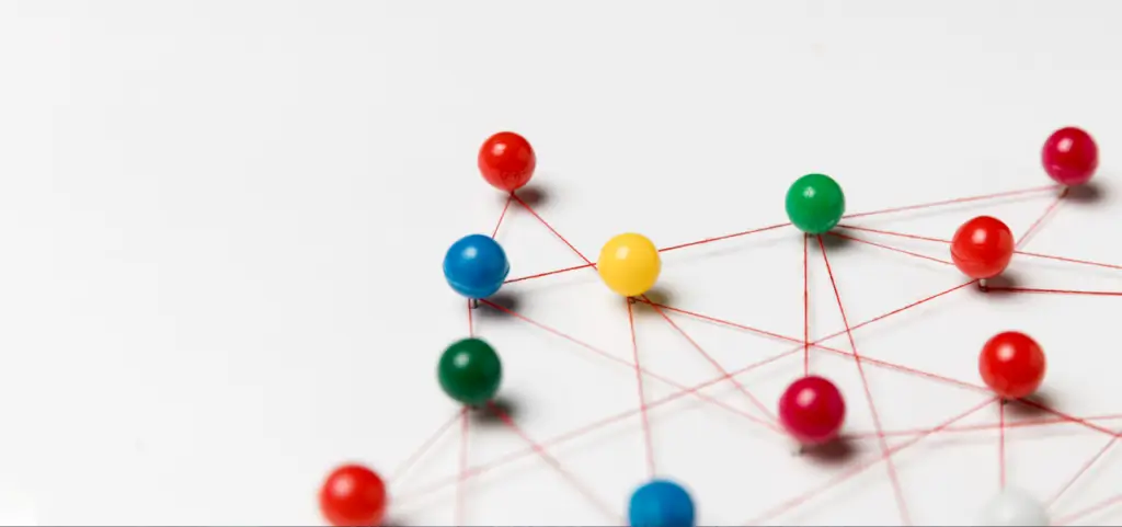 Coloured pushpins on a white surface joined by red string into a network of connected points
