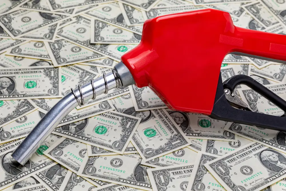 A red fuel nozzle lying on a scattered pile of dollar bills