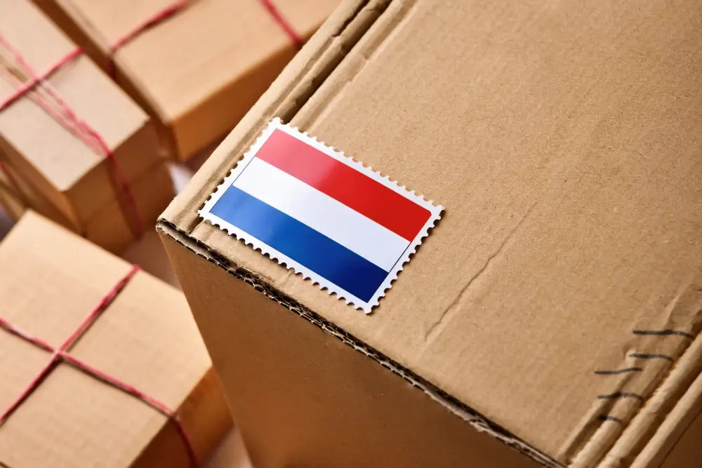 A Dutch flag postage stamp on the corner of a cardboard parcel, with more string-tied boxes behind it