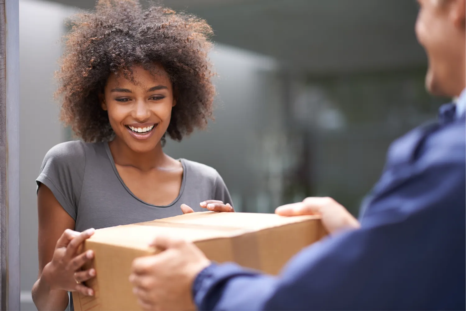 A smiling customer at the door taking a cardboard box from a courier in a navy uniform