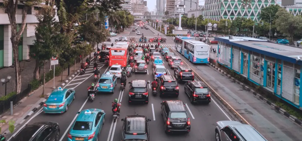 A multi-lane downtown street jammed with cars, taxis, buses and motorbikes between high-rise towers