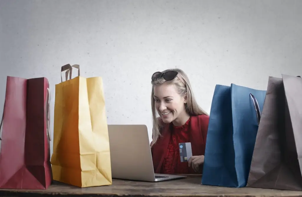 A shopper at a laptop holding a bank card, framed by paper shopping bags