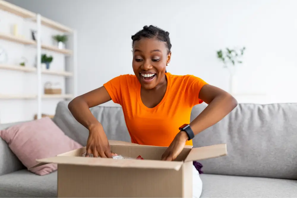 Someone on a sofa opening a cardboard parcel and smiling at what is inside