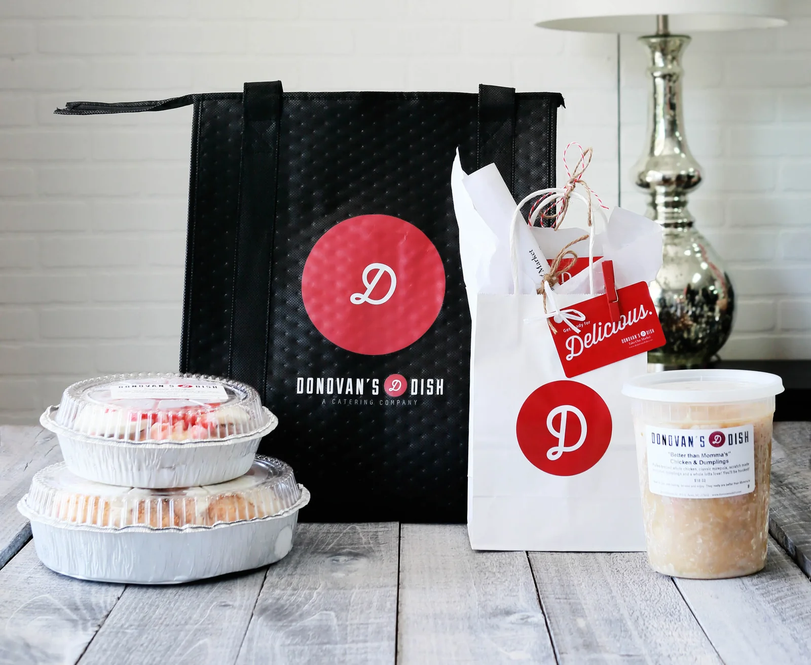 A Donovan's Dish insulated tote and gift bag beside foil pans and a tub of Better than Momma's chicken and dumplings