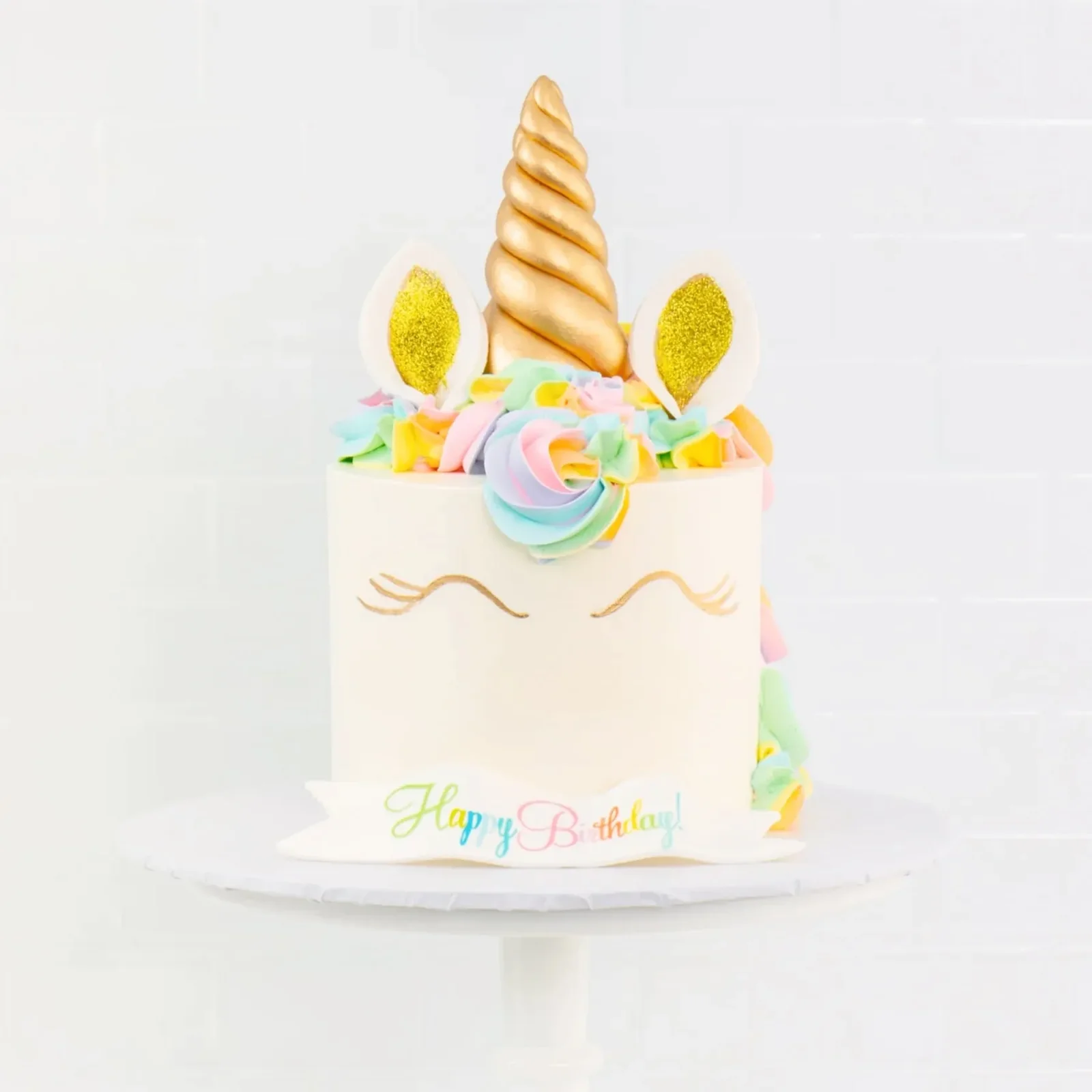 A Sweet E's unicorn birthday cake with a gold fondant horn, pastel buttercream mane and a Happy Birthday! banner