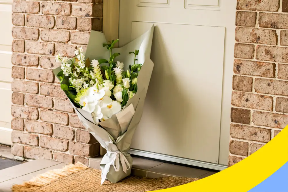A wrapped bouquet of white flowers left standing against a front door on a doormat