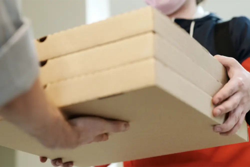 A masked courier passing a stack of flat cardboard boxes to a customer