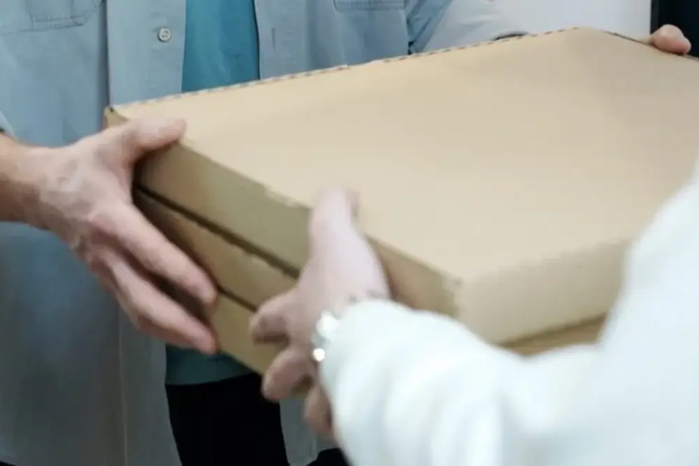 Two people passing a large flat cardboard box between them at a doorway
