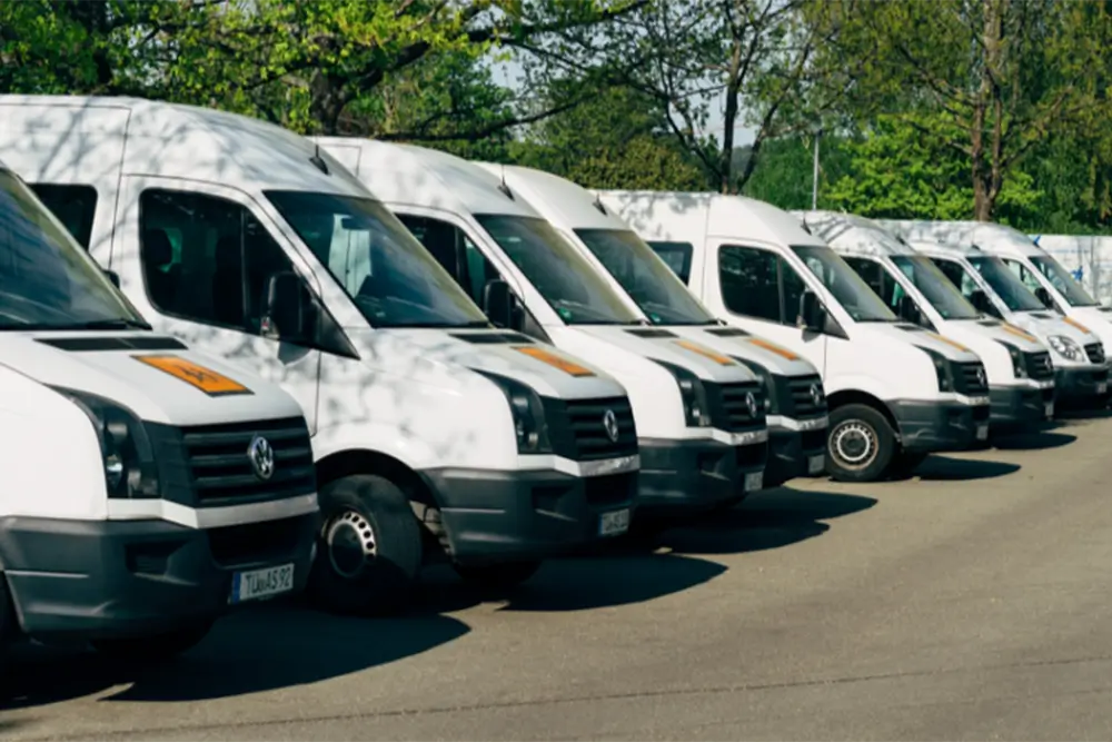 A row of identical white delivery vans parked nose-out in a depot yard