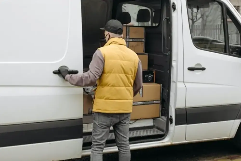 A courier in a yellow gilet opening the side door of a van packed with cartons