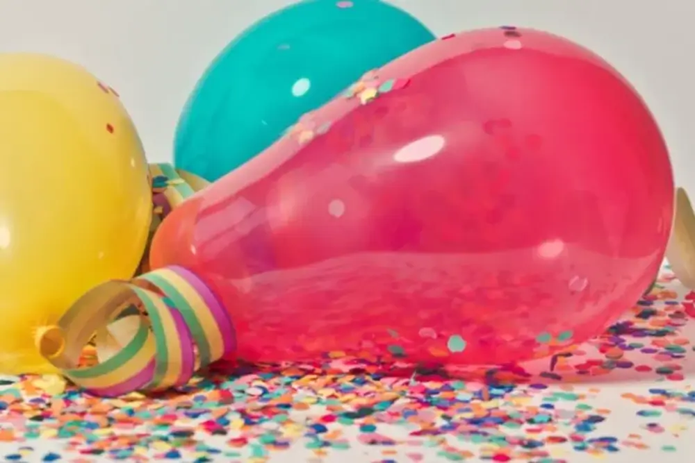 Yellow, teal and pink party balloons lying among scattered confetti and streamers