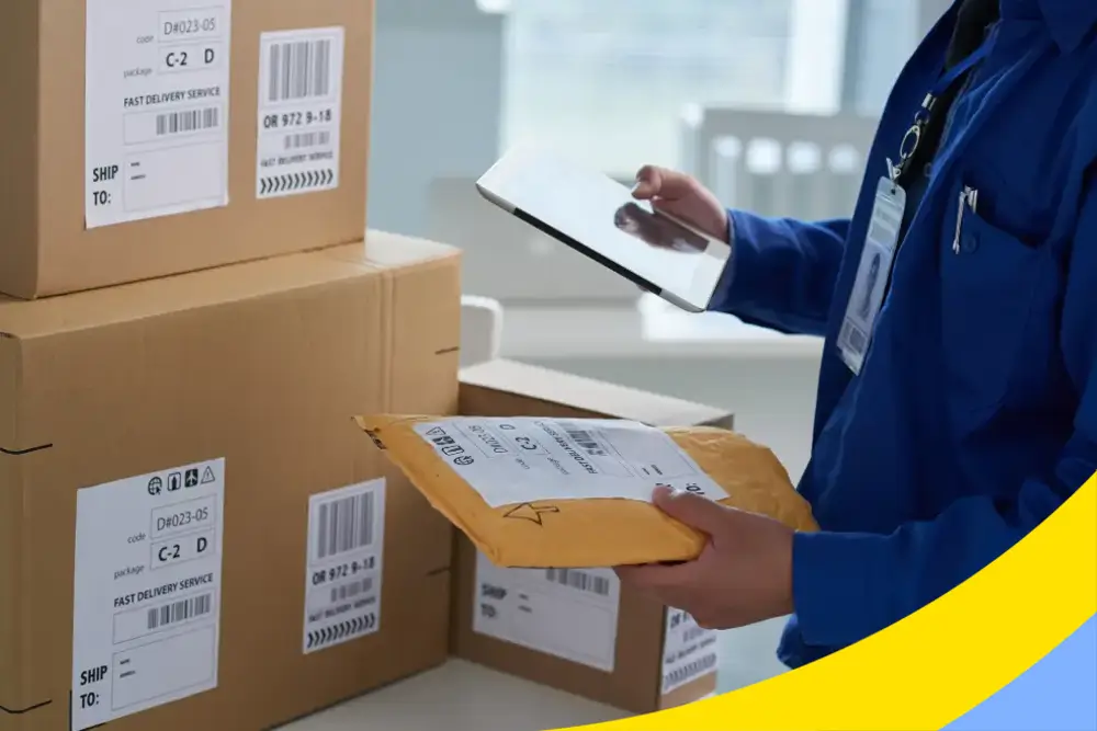 A courier in a blue uniform holding a tablet and a padded envelope beside labelled cartons