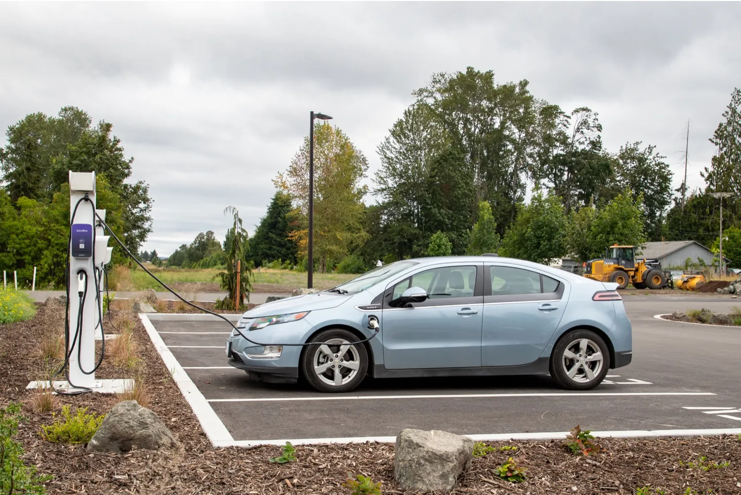 A pale blue electric car plugged into a charging post in a car park