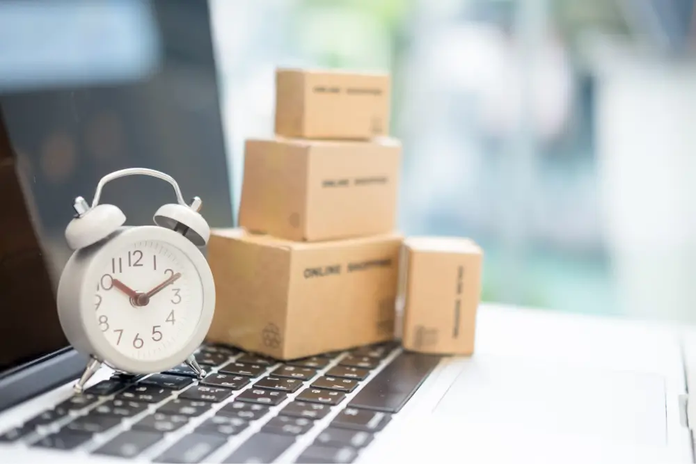 A small alarm clock on a laptop keyboard beside a stack of parcels