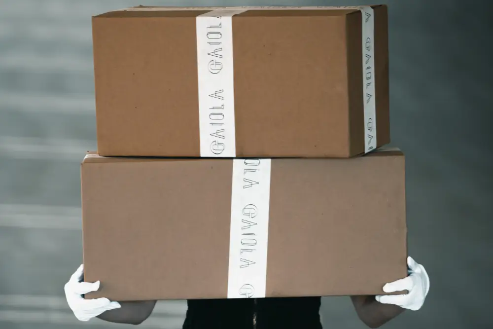 A courier in white gloves carrying two taped cartons stacked in front of them