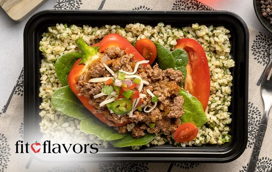 A fit-flavors meal container of stuffed red pepper with ground beef, spinach and tomatoes on a bed of grains, with the fit-flavors logo