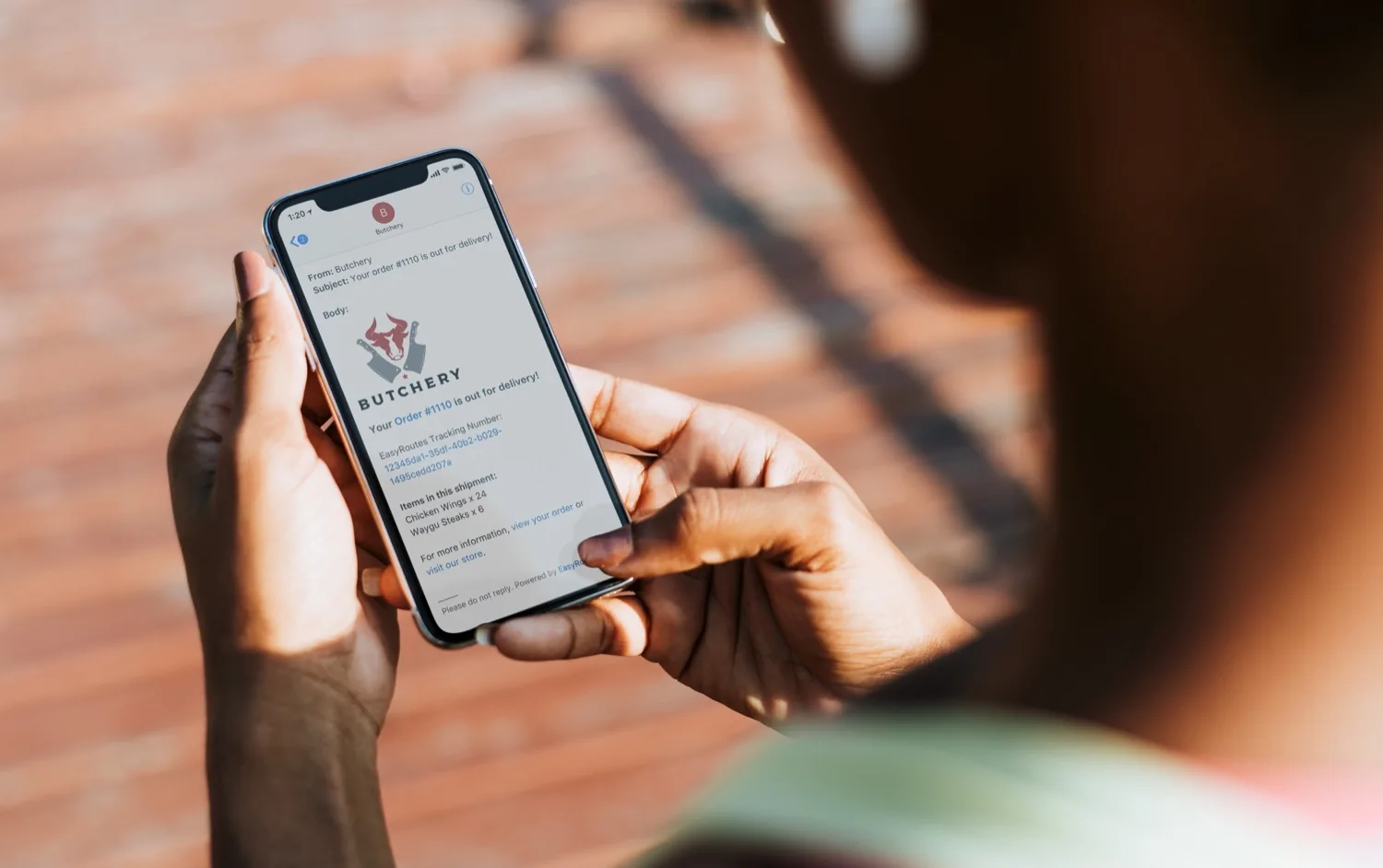 A person holding a phone showing a store's “Your order #1110 is out for delivery!” email with a tracking number and item list